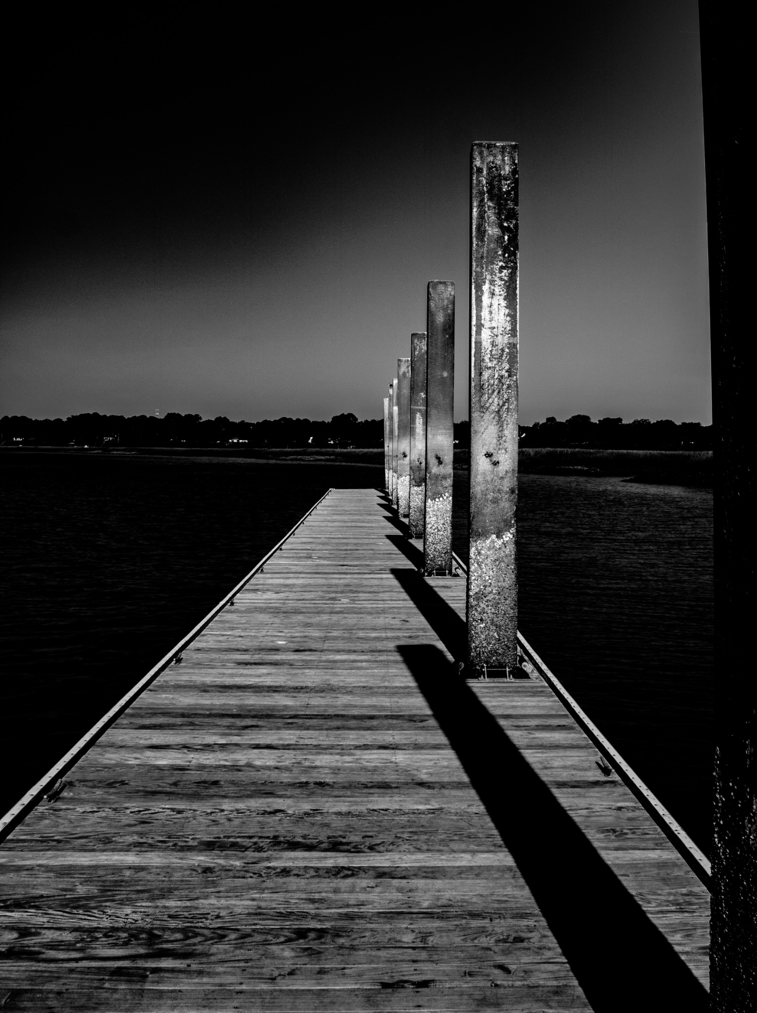 An empty dock extending toward a single vertical piling and distant water