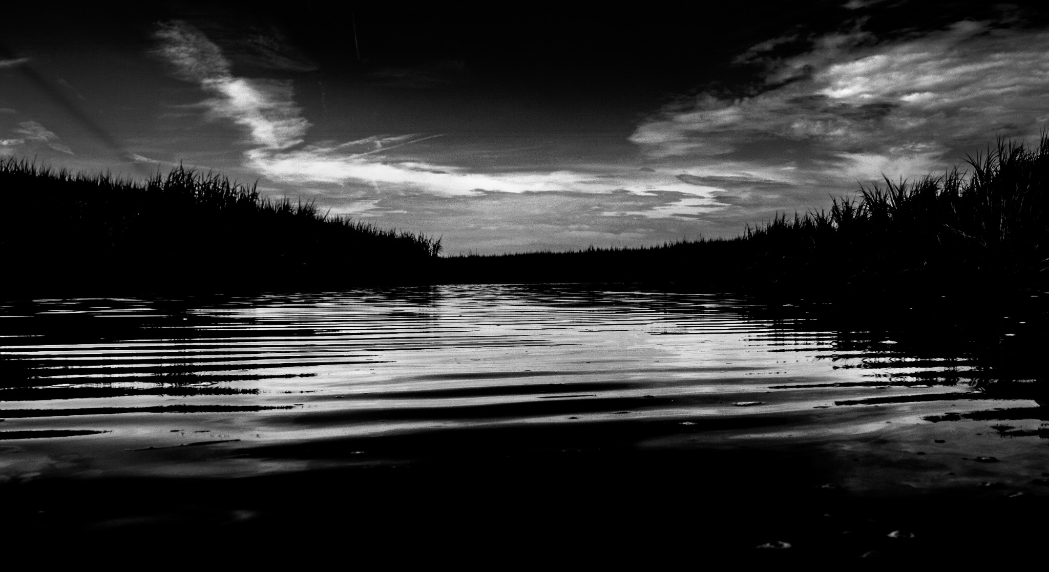 Dark water and a distant shoreline beneath a luminous break in the sky